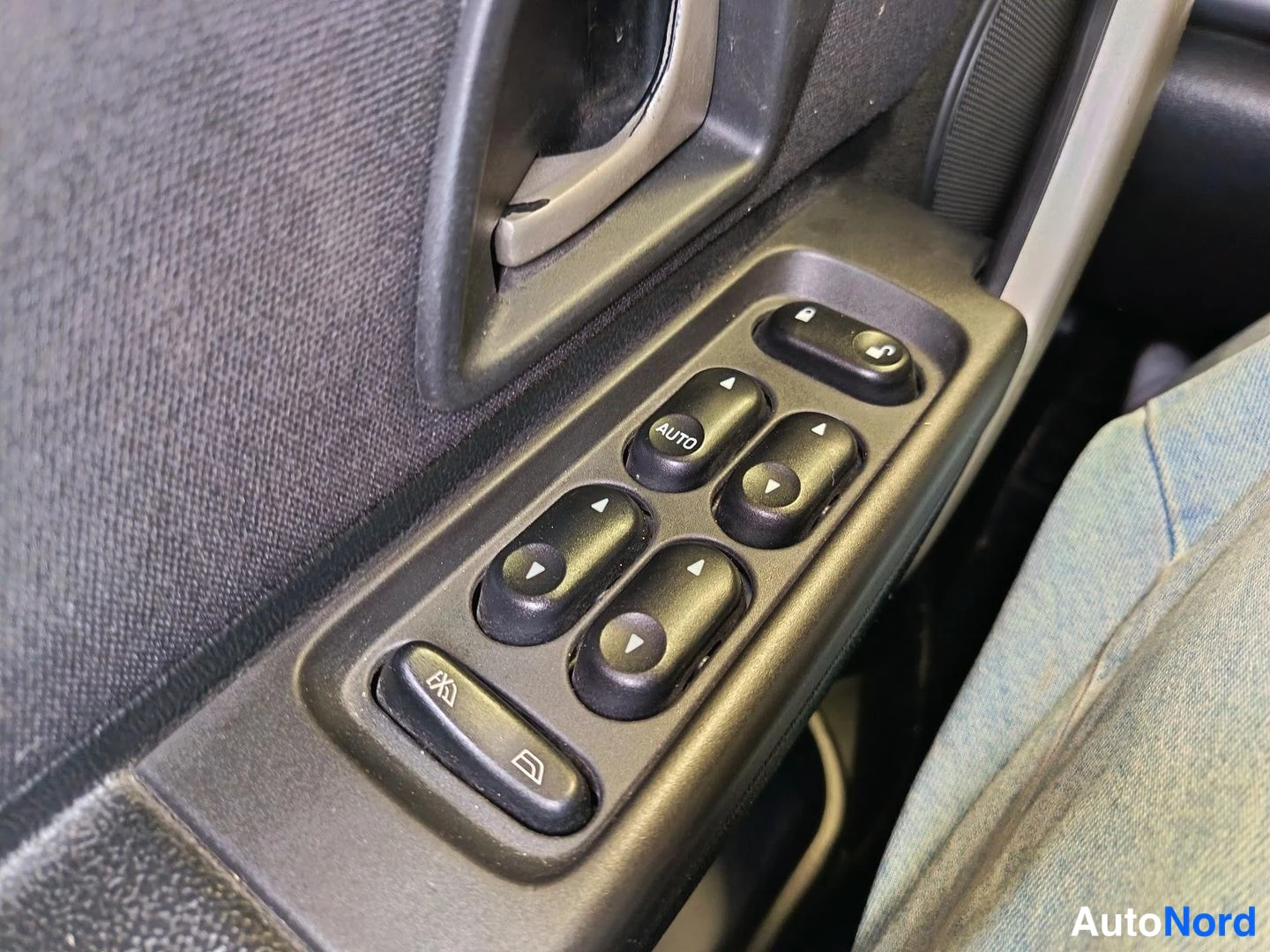 Yksityiskohta: Driver’s door control panel close-up featuring black plastic trim with five switches arranged vertically: window lock at top, single AUTO button for front windo