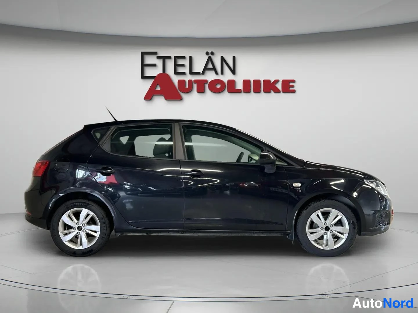 Sivulta: Musta viisiovinen hatchback sivulta kuvattuna studio-oloissa, hopeanvalkoiset pyörät.