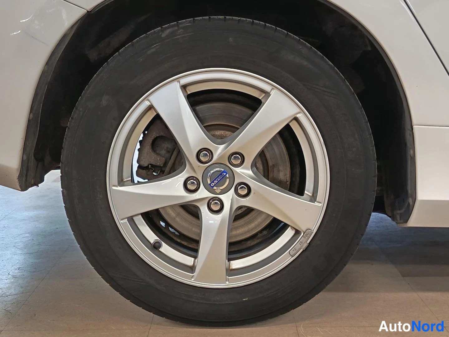 Sivulta: Lähikuva auton valkoisesta karossaarista: hopea viisikuvioinen Volvo-vanne ja musta rengas.