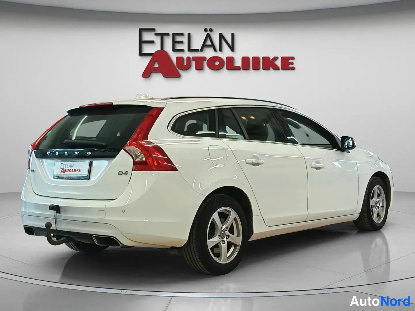 Takaviisto: Valkoisen Volvo V60 -farmariauton takaosa ja oikea kylki kolmeneljänneskulmasta; vetokoulu ja hopeat kevytmetallivanteet näkyvät.