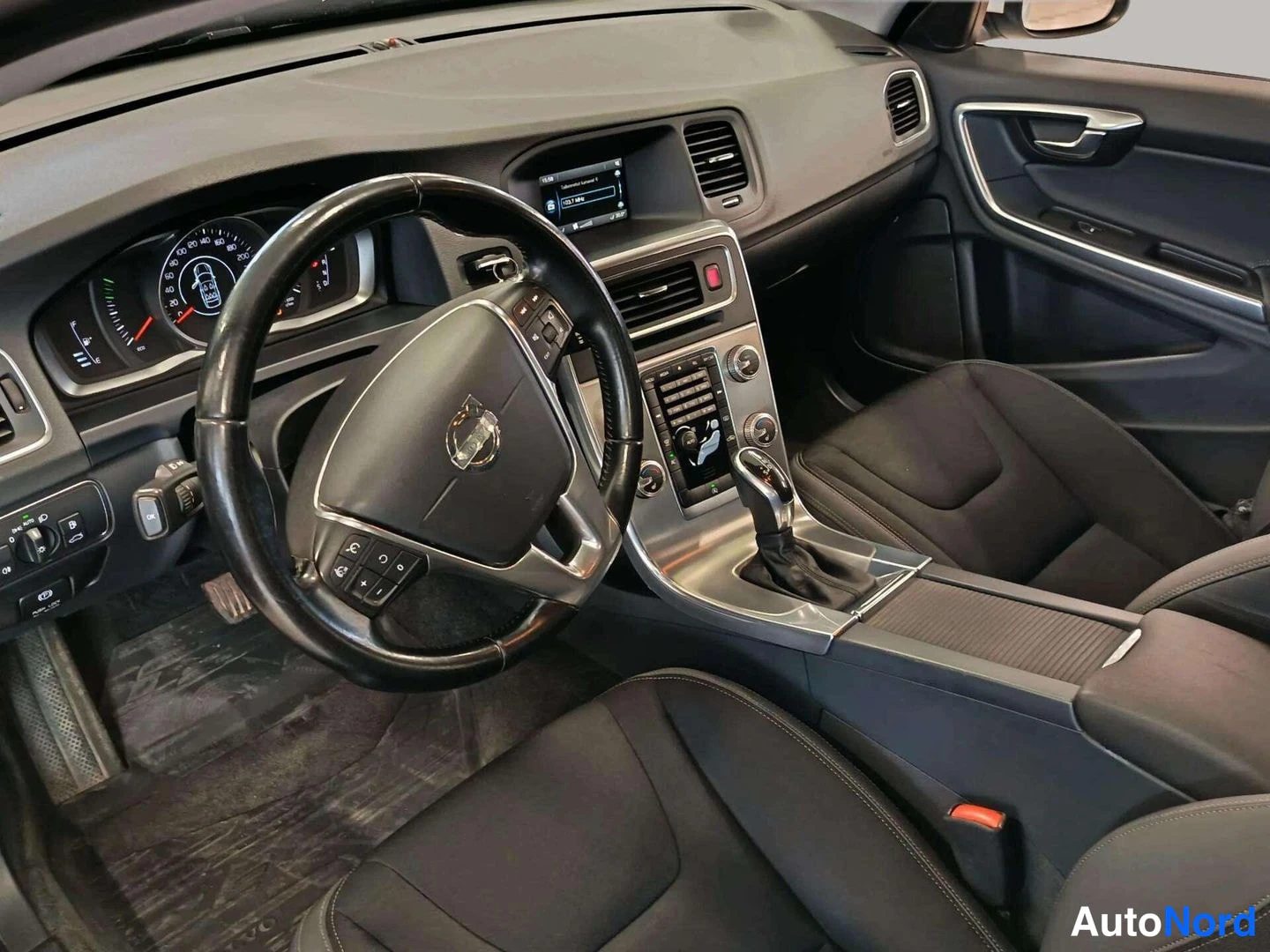 Muu: Volvo V60:n ohjaamo kuljettajan puolen suunnasta: ohjauspyörä, mittaristo, infotainment-näyttö, automaattivaihteen valitsin ja tummat istuimet.