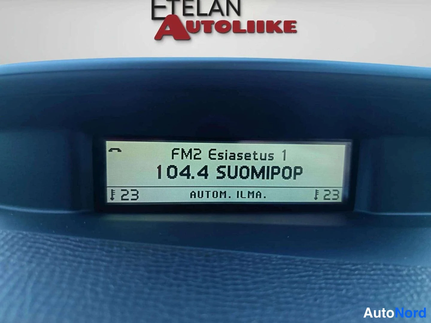 Muu: Kojeiston infonÃ¤yttÃ¶, jossa teksti 'FM2 Esiasetus 1 / 104.4 SUOMIPOP / 23 AUTOM. ILMA. 23'. YlÃ¤osassa markkinoitsijan logo ETELÃN AUTOLIIKE.