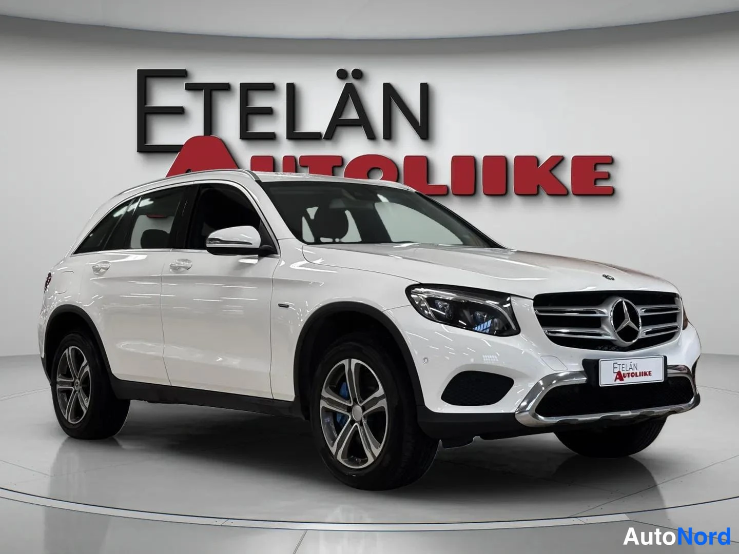 Etuviisto, nokka oikealle: Valkoinen Mercedes-Benz GLC -maasturin etukulmanäkuva autonhallissa, kylki ja etusäleikkö näkyvissä.