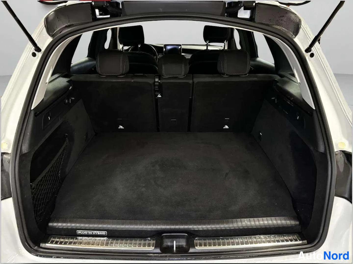 Muu: Auton tavaratila avatusta takaluukusta kuvattuna, tumma matto ja taitetut takaselkänojat; kotelossa PLUG-IN HYBRID -teksti.
