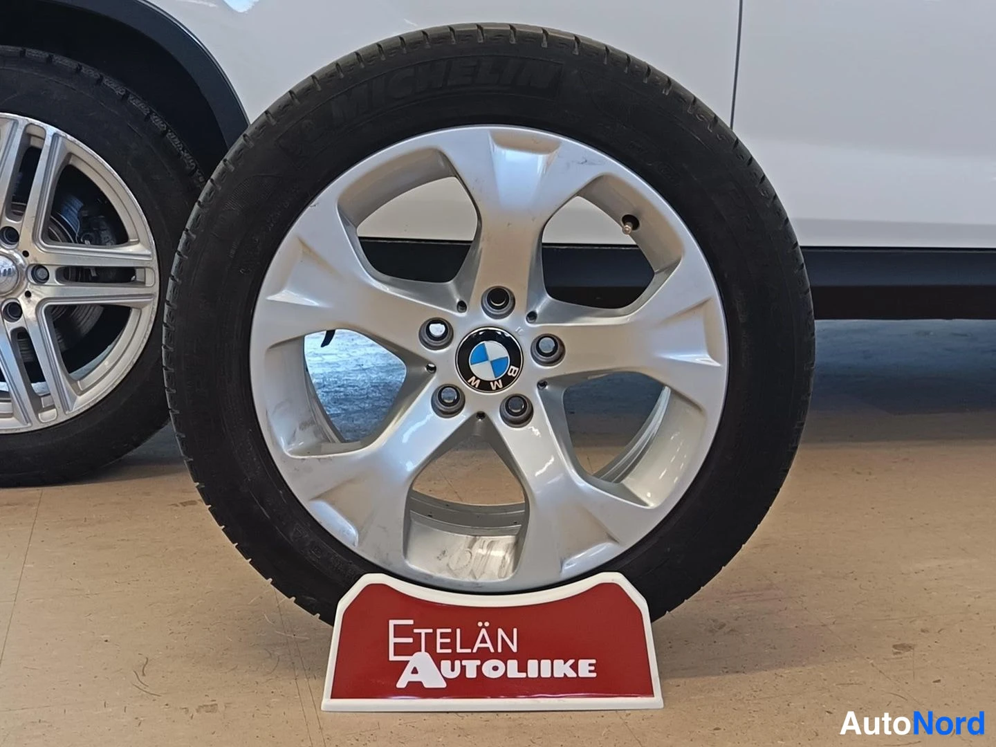 Yksityiskohta: Hopeanvärinen viisipuolainen BMW-vanne nokalla, Michelin-rengas, auton kylki taustalla.