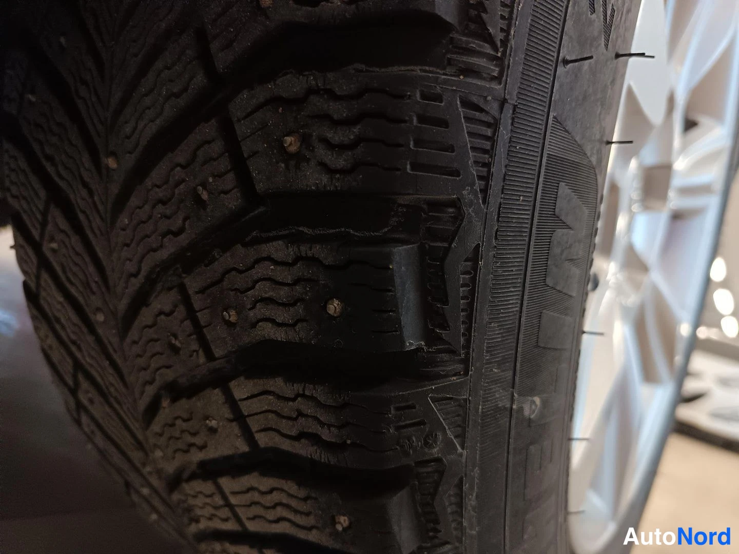 Yksityiskohta: Close-up of a studded winter tyre tread and sidewall.