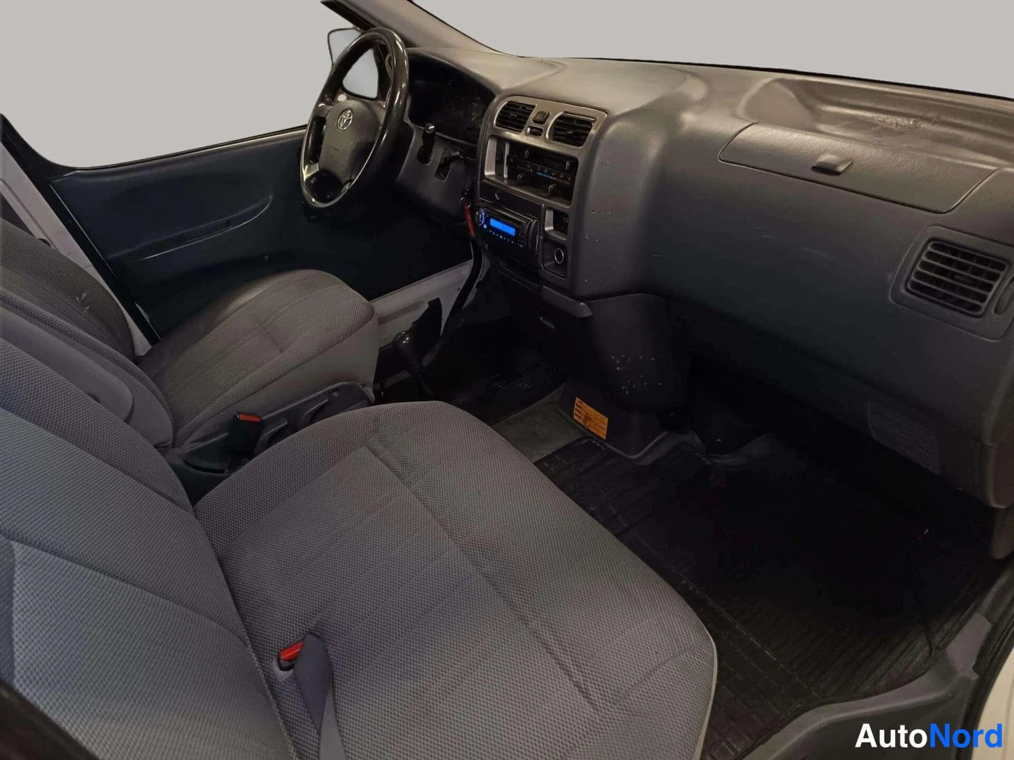 Muu: Auton sisätilat kojelaudasta taakse: Toyota-ohjauspyörä, radio sinisellä näytöllä ja harmaat istuimet.