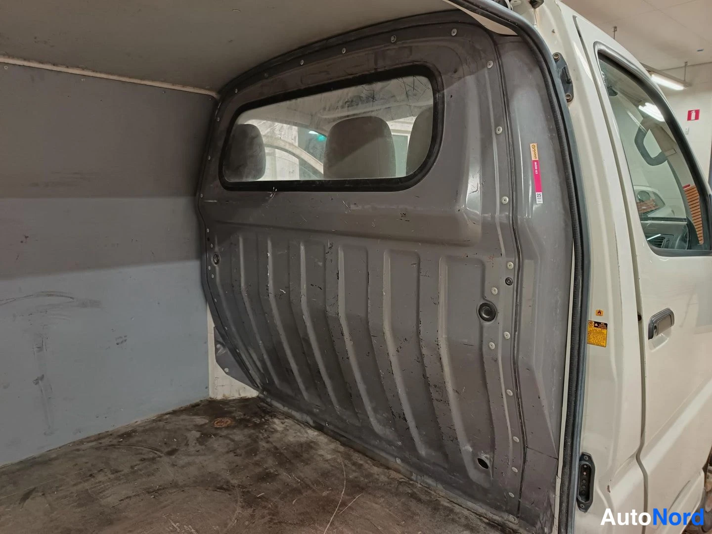 Tavaratila: Interior shot showing the metal cargo partition separating driver cabin from load space. Partition has a rectangular cutout window allowing visibility into cabi