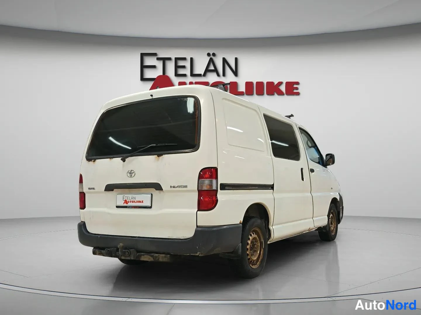 Takaviisto: Toyota Hiace -pakettiauto takaa oikealta viistosti valkoisena studiovalaistuksessa.