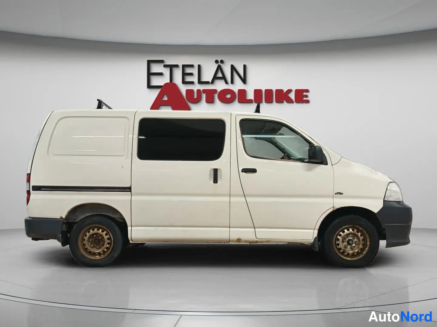 Etuviisto, nokka oikealle: Toyota Hiace -pakettiauto sivulta edestä oikealta valkoisena studiovalaistuksessa.