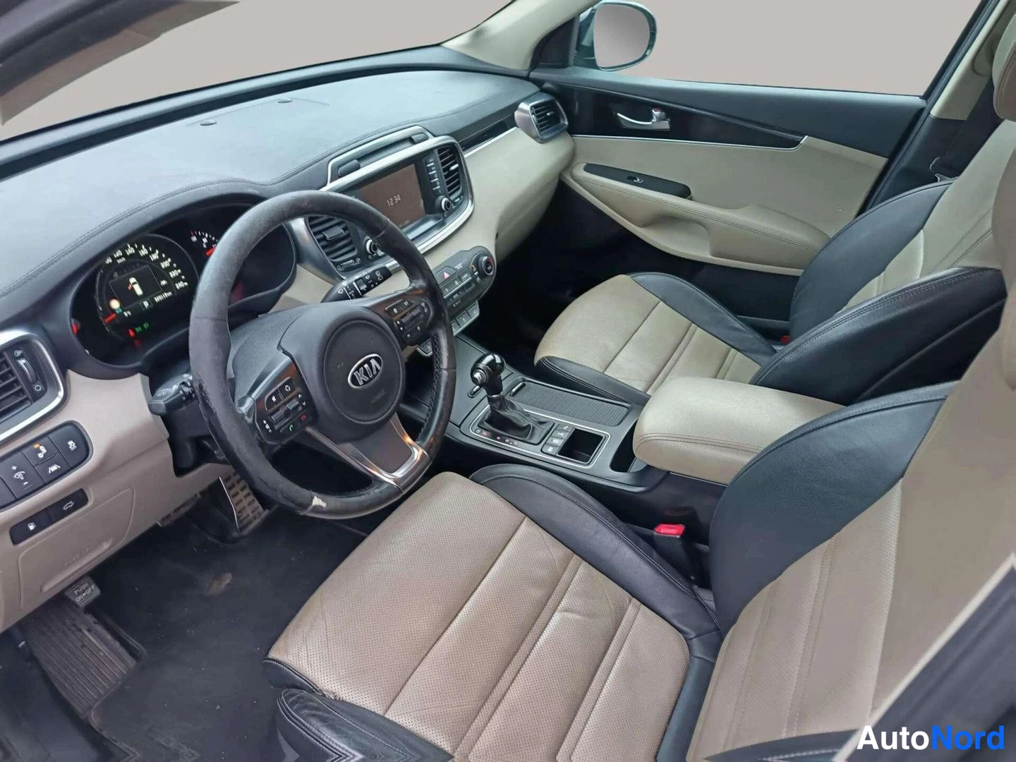 Edestä: Kia:n auton sisätilat: beige-mustat penkit, ohjauspyörä ja keskikonsoli automaattivaihteistolla ja kosketusnäytöllä.