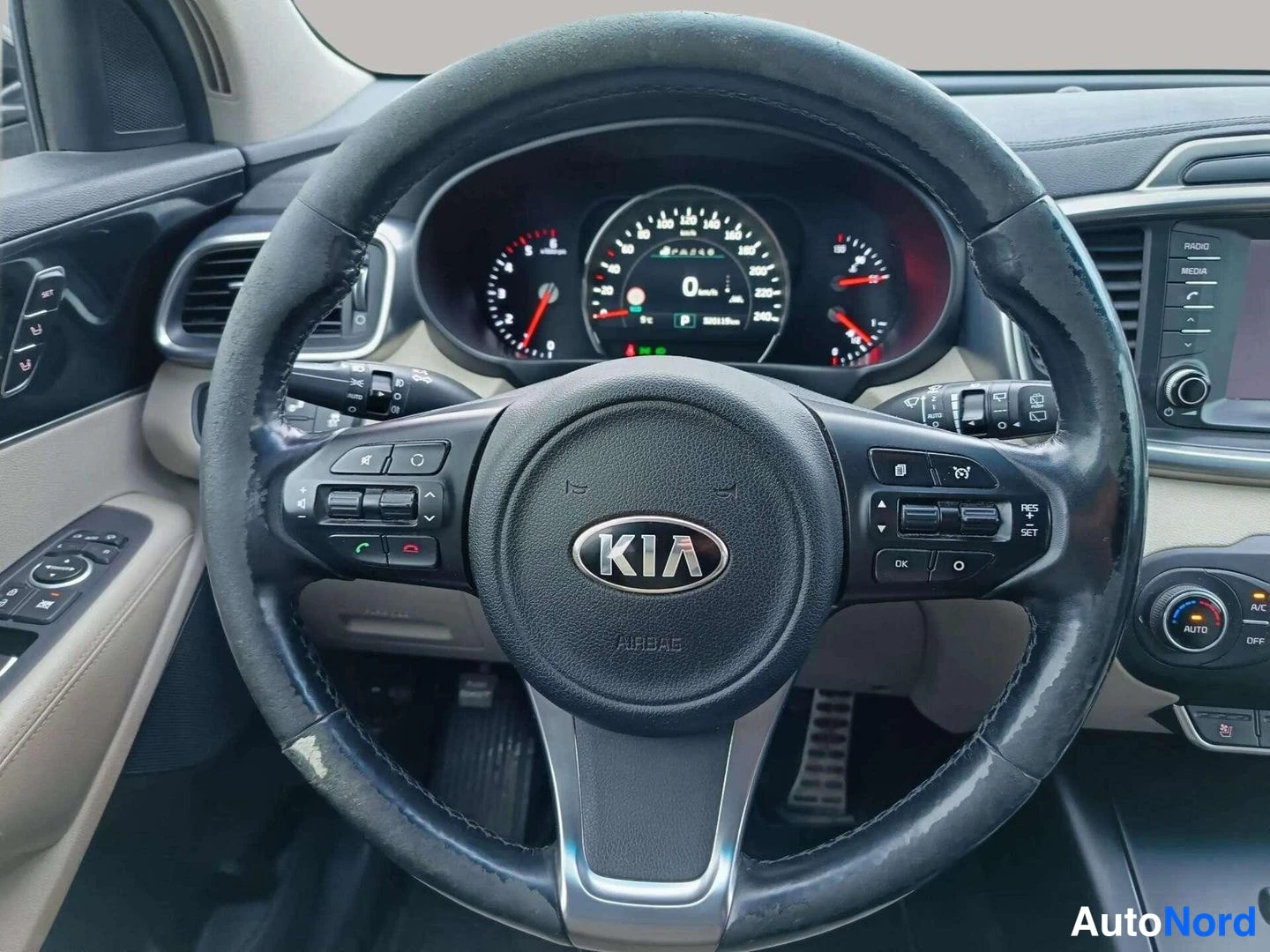 Edestä: Ohjauspyörän lähikuva, KIA-merkki ja AIRBAG-teksti keskellä, mittaristo taustalla näyttää 0 km/h.