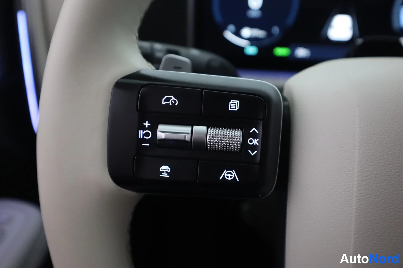 Yksityiskohta: Ratin pikanäppäimet lähikuvassa: cruise control -painikkeet, rulla ja OK-nappi, taustalla kojelauta.