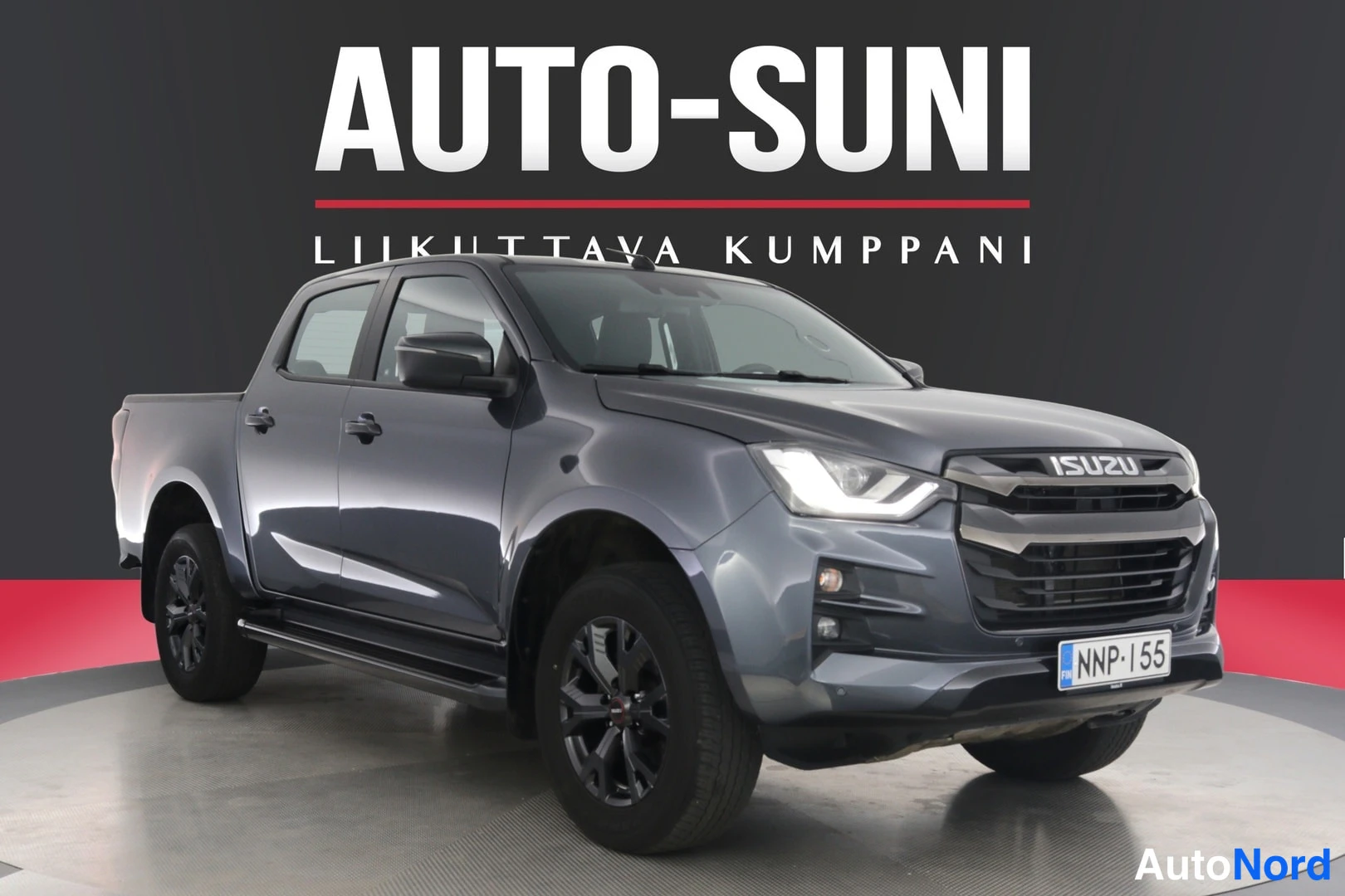 Etuviisto, nokka oikealle: Isuzu D-Max -pakettiauto edestä vasemmalta kuvattuna, tummanharmaa, Auto-Suni-myymälätausta.
