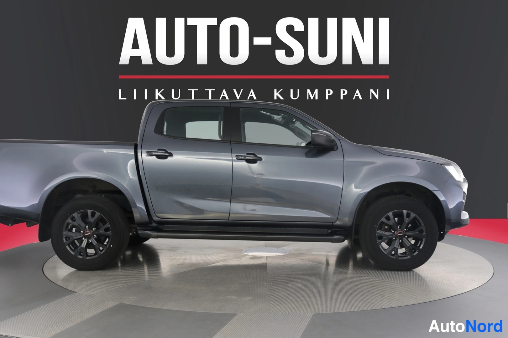 Etuviisto, nokka oikealle: Isuzu D-Max sivulta kuvattuna, tummanharmaa korimalli studioitaustaa vasten.