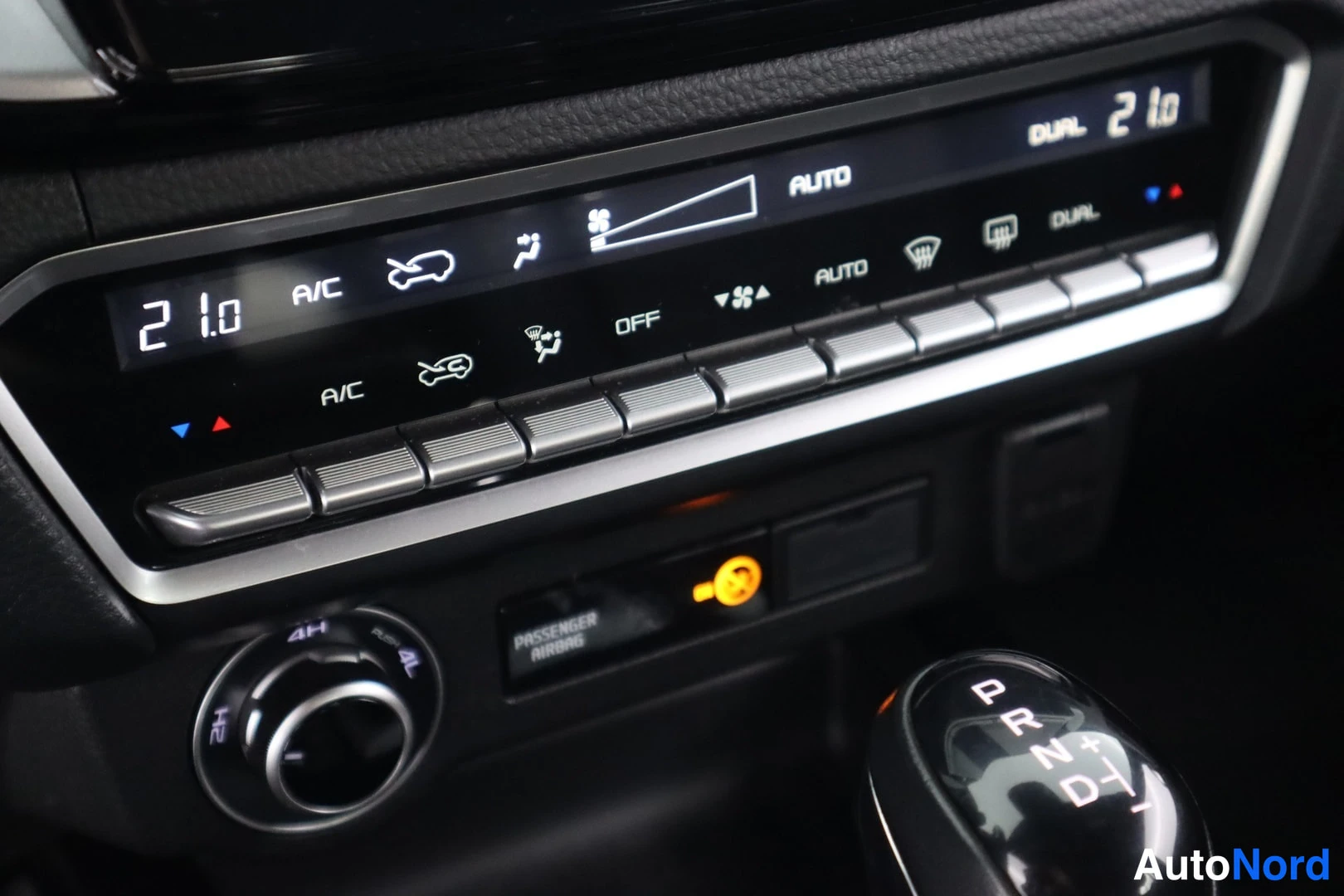 Yksityiskohta: Auton keskikonsoli: ilmastointilaitteen (AC, AUTO, DUAL) näyttö ja painikkeet, nelivetovalitsin (4H, 4L, 2H) ja automaattivaihteen valitsin.
