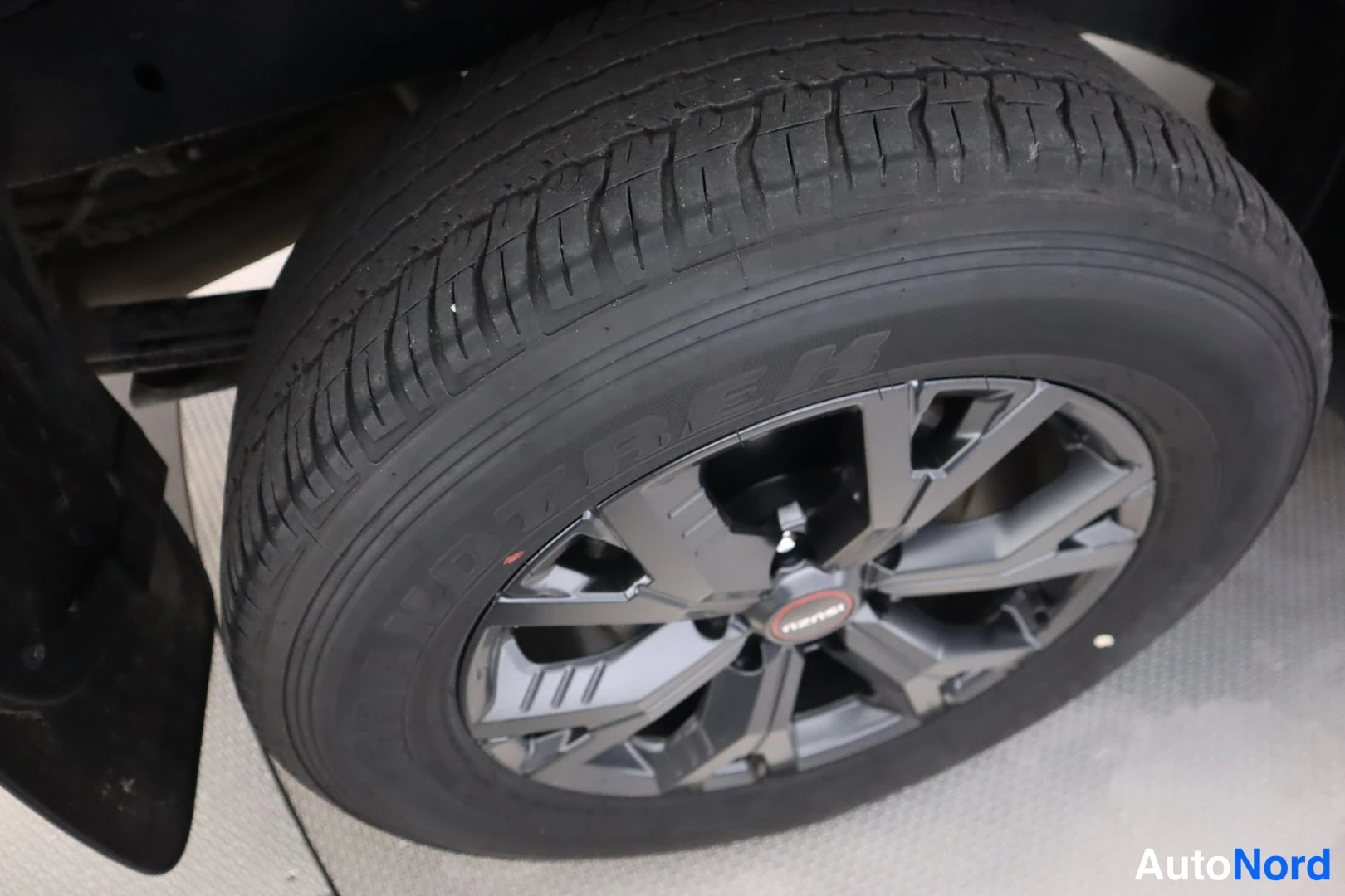 Yksityiskohta: Yksityiskohta auton takarenkaasta ja tummasta kevytmetallivanteesta,.Isuzu-merkitty napa.