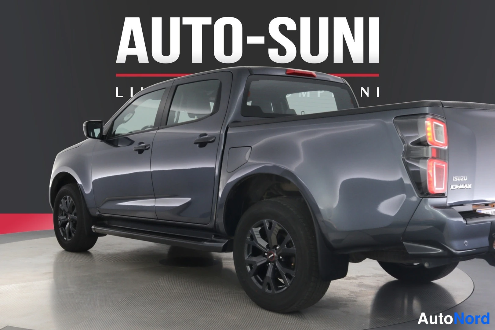 Takaviisto: Isuzu D-Max takaa oikealta kuvattuna, tummanharmaa korimalli, D-Max-teksti lavan sivussa.