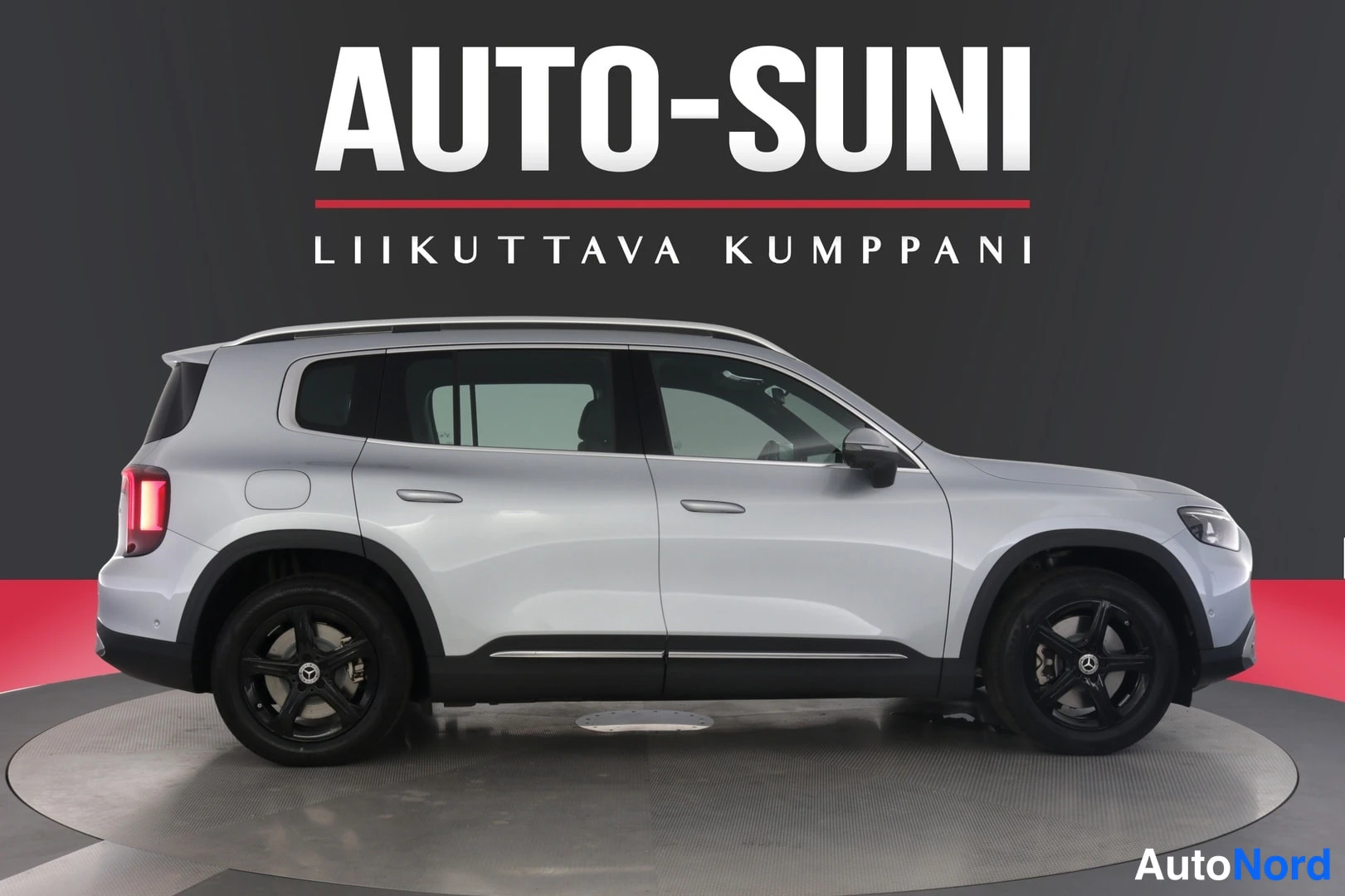 Sivulta: Profile shot of the vehicle's left flank featuring black wheels and silver paintwork against a dark background.