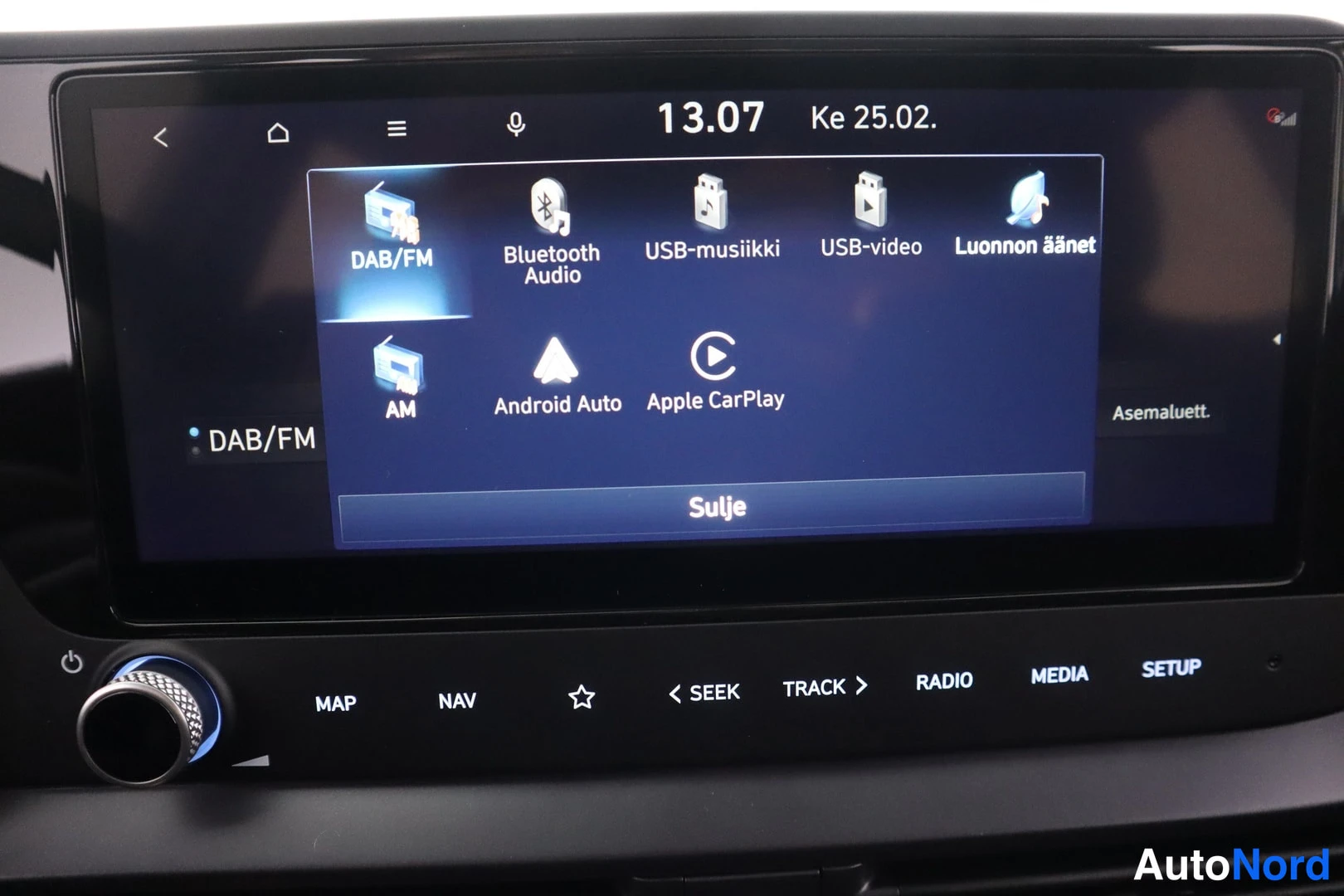 Edestä: Autojen infotainment-näyttö, jonka valikossa vaihtoehdot DAB/FM, Bluetooth Audio, USB-musiikki, USB-video, Luonnon äänet, AM, Android Auto ja Apple CarPlay.
