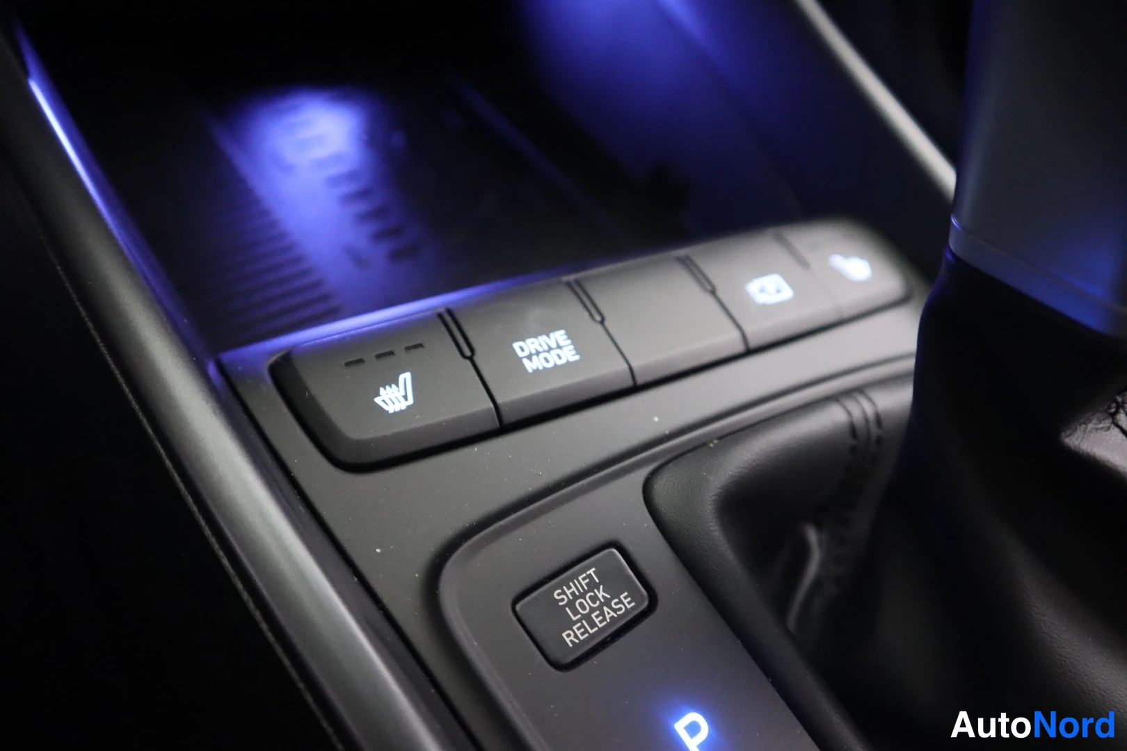 Edestä: Auton keskuskonsolin painikkeet DRIVE MODE ja SHIFT LOCK RELEASE -napilla sinisessä tunneloituksessa.