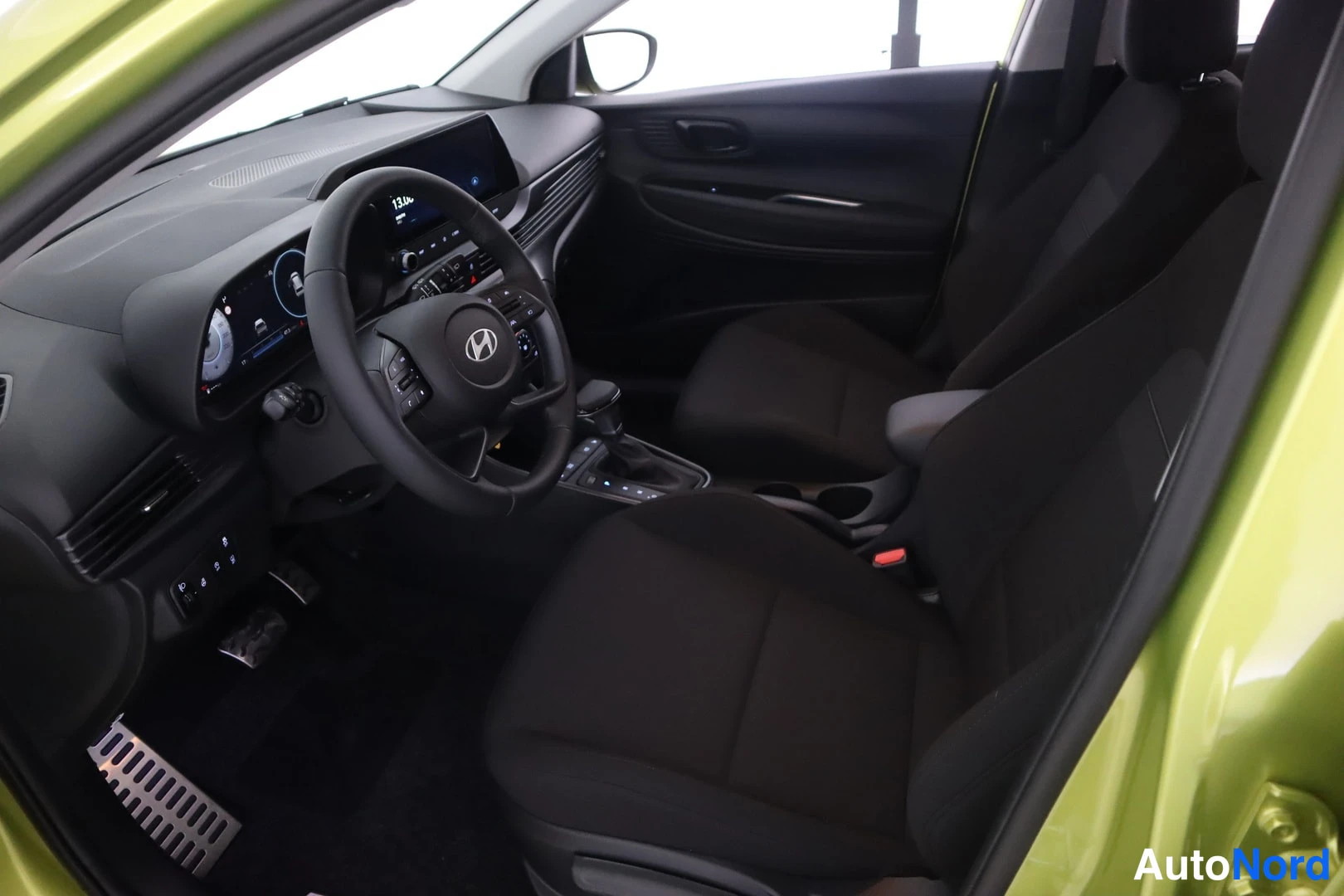 Ohjaamo: Wide interior shot from passenger door opening showing driver seat, dashboard layout, center console with gear shifter, passenger seat, and air vents.
