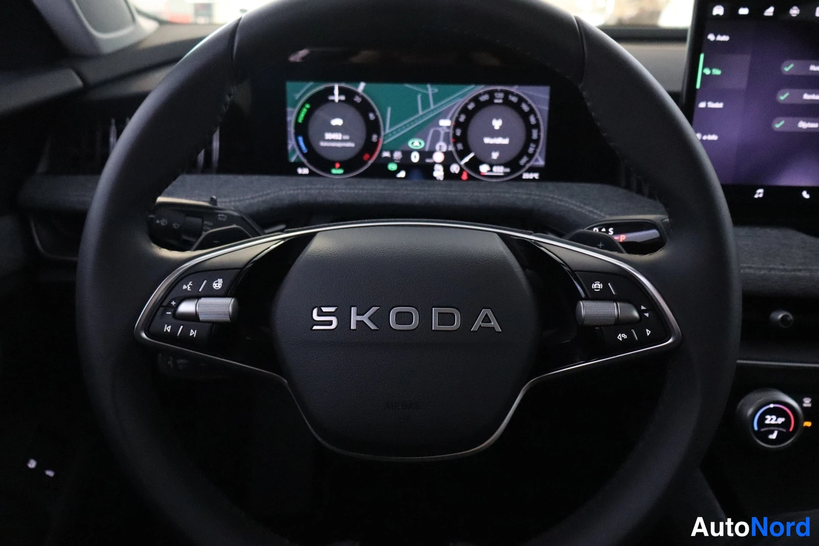 Ohjaamo: Ohjauspyörä kuvattuna lähikuvasta, jossa on Skoda-logo keskellä. Digitaalinen mittaristo näkyy taustalla.