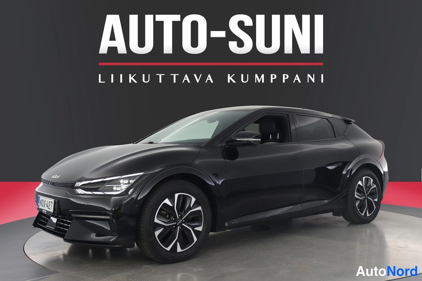 Etuviisto, nokka vasemmalle: Musta Kia EV6 etuokolmaisesta kulmastä kuvattuna myyntihallissa, Auto-Suni-taustalla rekisterikilpi.