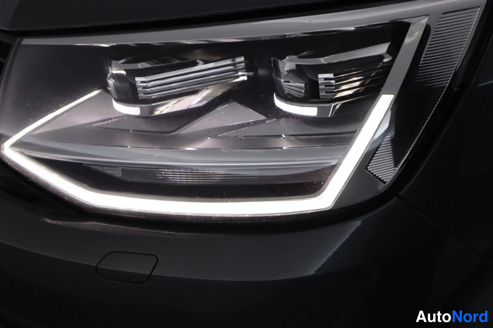 Edestä: Lähikuva Volkswagenin tumman mustasta etuletusta: LED-ajovalo, jonka päiväaika-valot palavat, sekä osa etusäleiköstä.