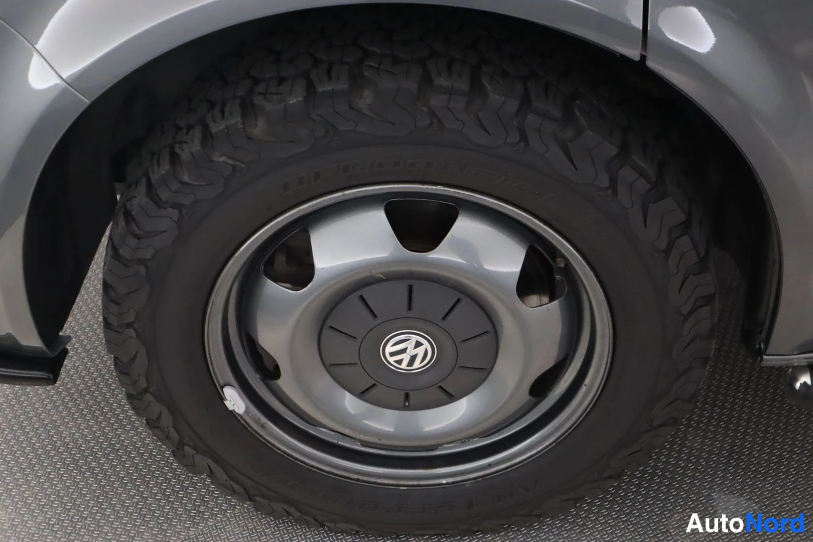 Yksityiskohta: Lähikuva Volkswagenin takarenkaasta ja terttipyyhkäisyllä varustetusta teräsvanteesta, jossa VW-merkki keskellä. Karkeapalkkinen BFGoodrich-renkaallinen.