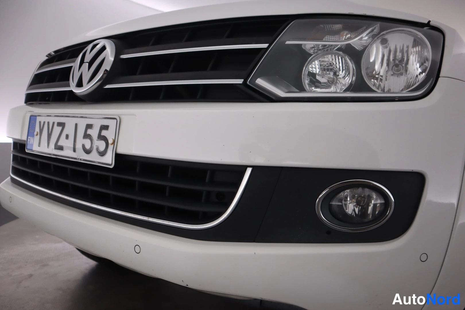 Edestä: Kuva autoa: valkoisen auton etuosan lähikuva, VW-merkki, etukisko, rekisteritunnus, ajovalo ja sumuvalo näkyvät.