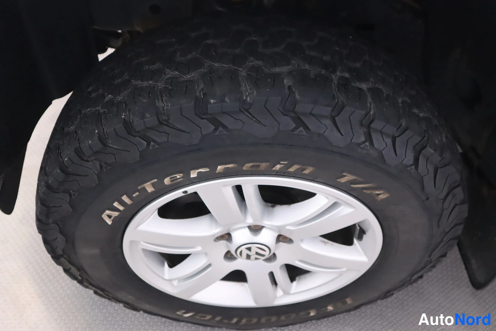 Yksityiskohta: Lähikuva mustasta BFGoodrich All-Terrain T/A -renkaasta ja hopeavanteesta, jonka keskellä on Volkswagen-merkki.