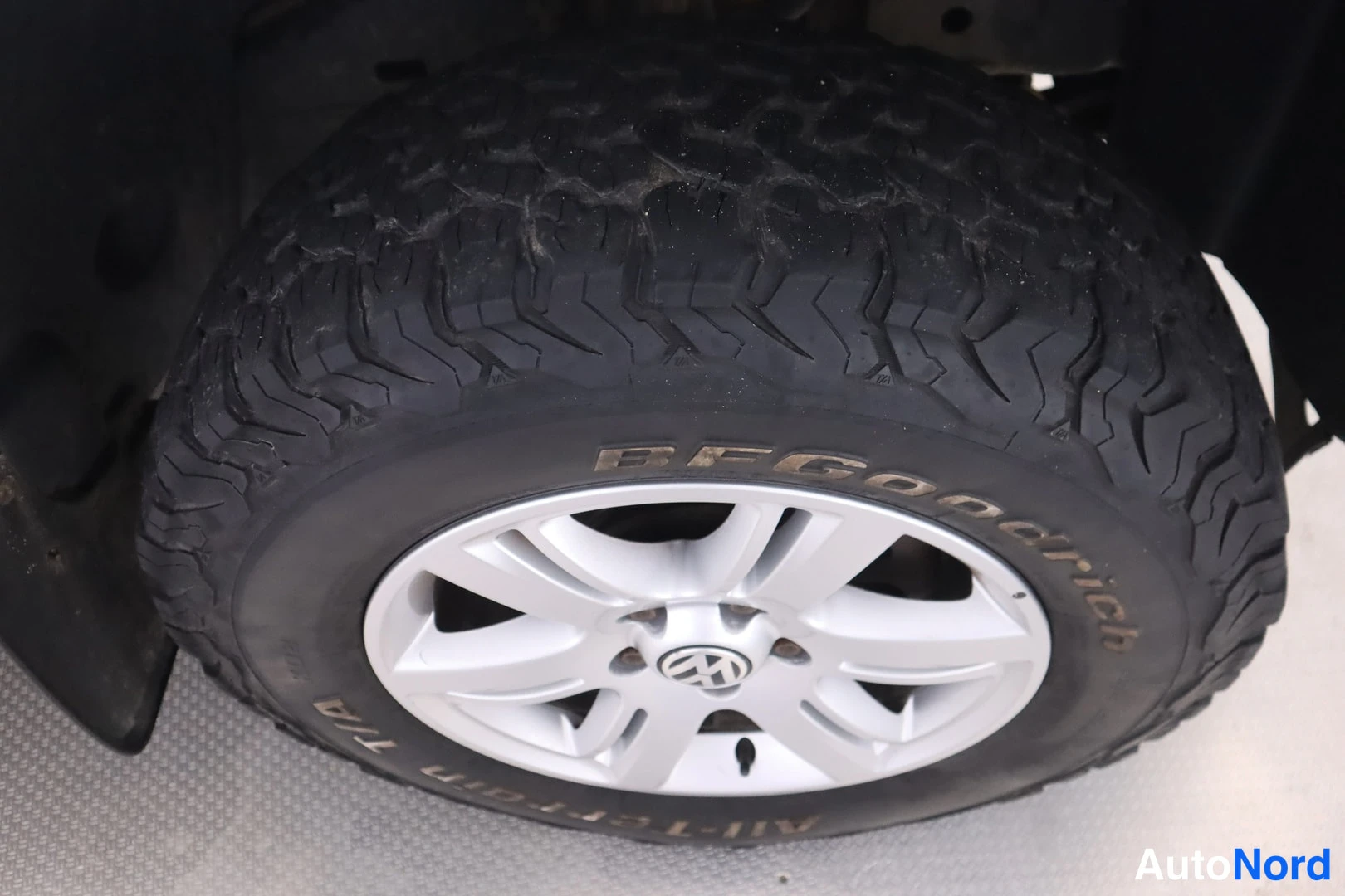 Yksityiskohta: Lähikuva BFGoodrich All-Terrain T/A -renkaasta ja hopeasta viisipuikkovanteesta Volkswagen-merkillä.