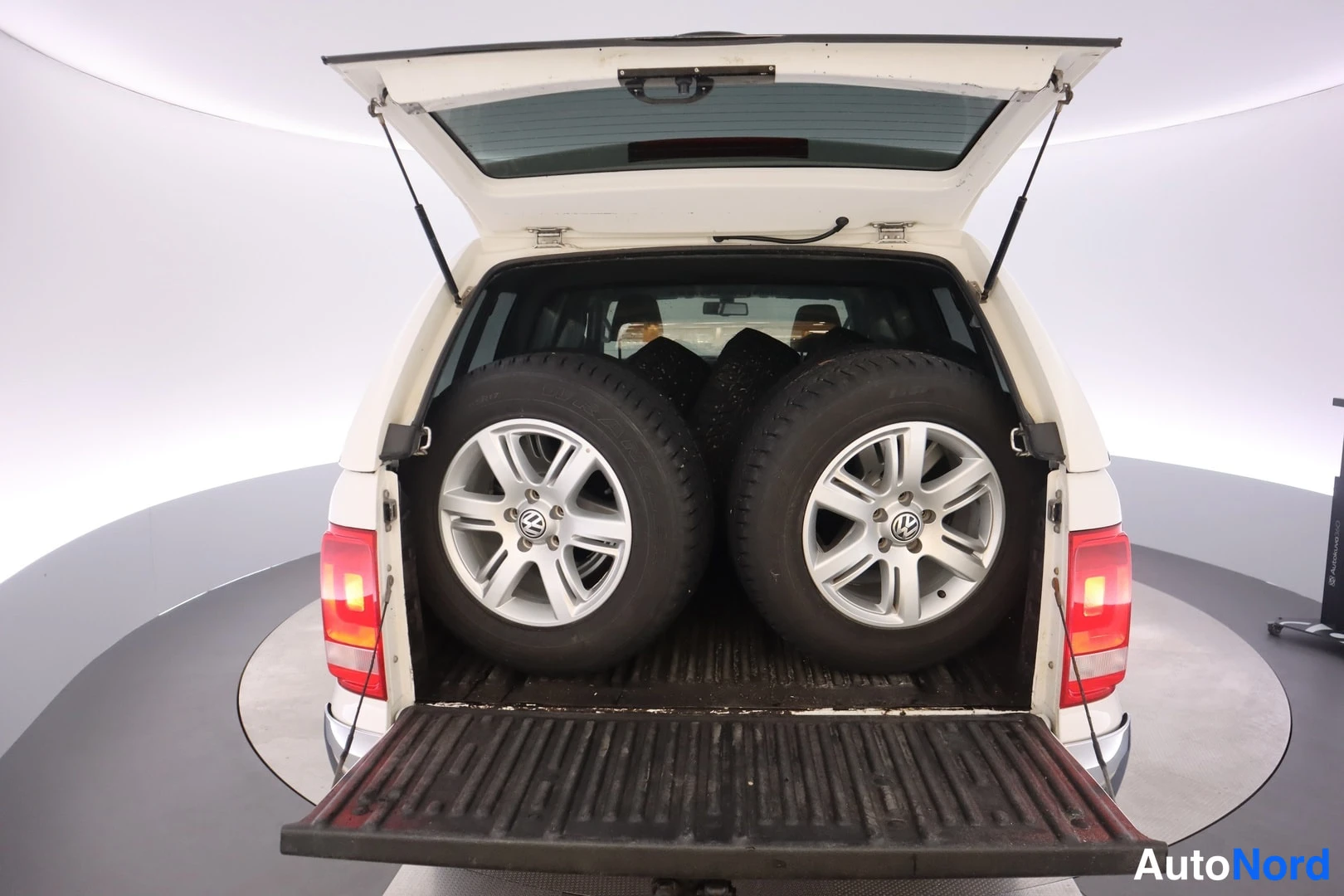 Takaa: Auton takanäkymä: avattu lavan kansi auki, tavaratilassa kaksi vararellasta VW-vanteilla, laskutettu lavanportti ja punaiset takavalot näkyvissä.