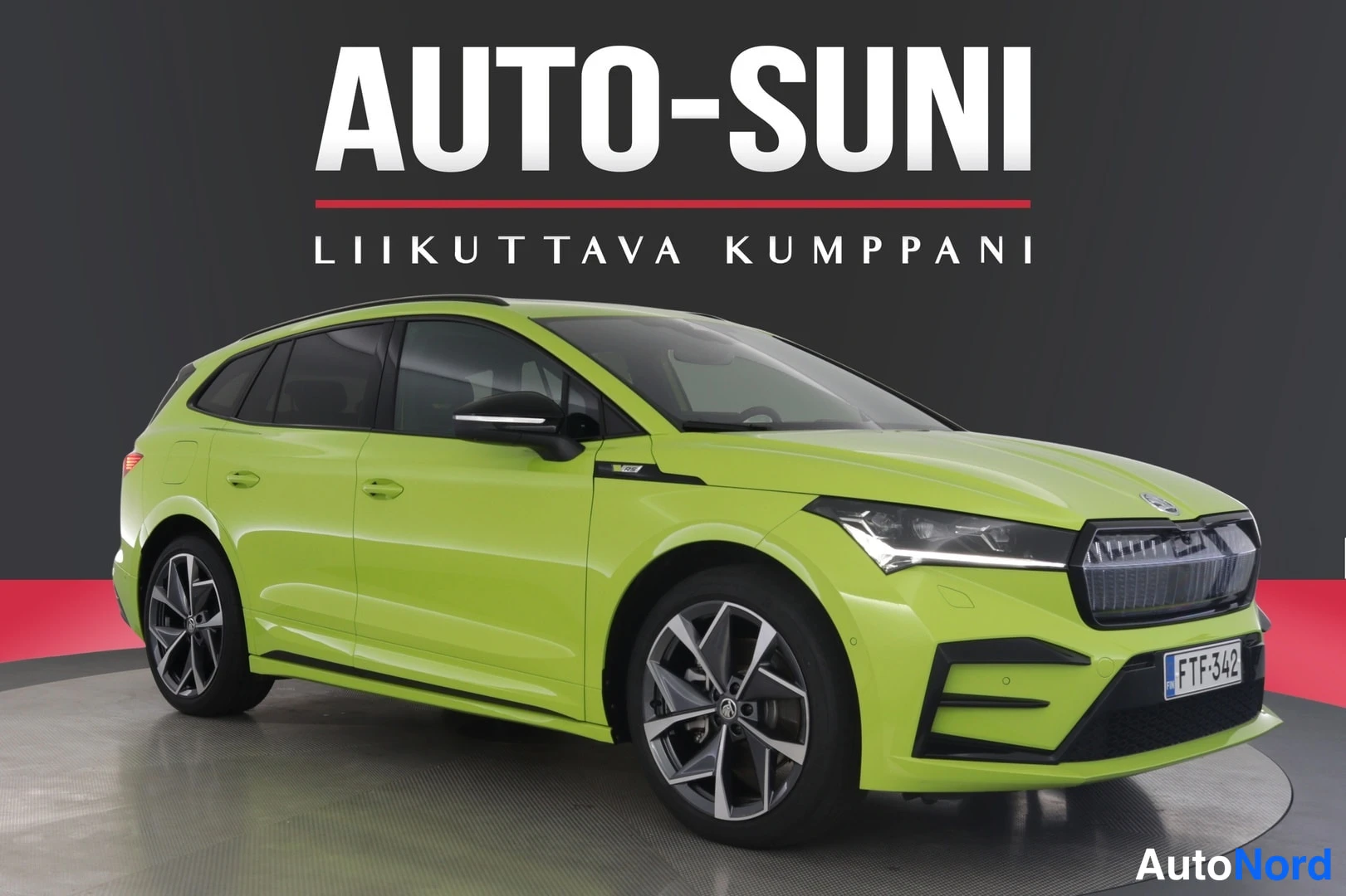 Etuviisto, nokka oikealle: Kirkkaan vihreä farmariauto autonmyyntistudiossa, etukulmanäkyvyys oikealle, rekisterikilpi, taustalla musta seinä ja punainen kaista.