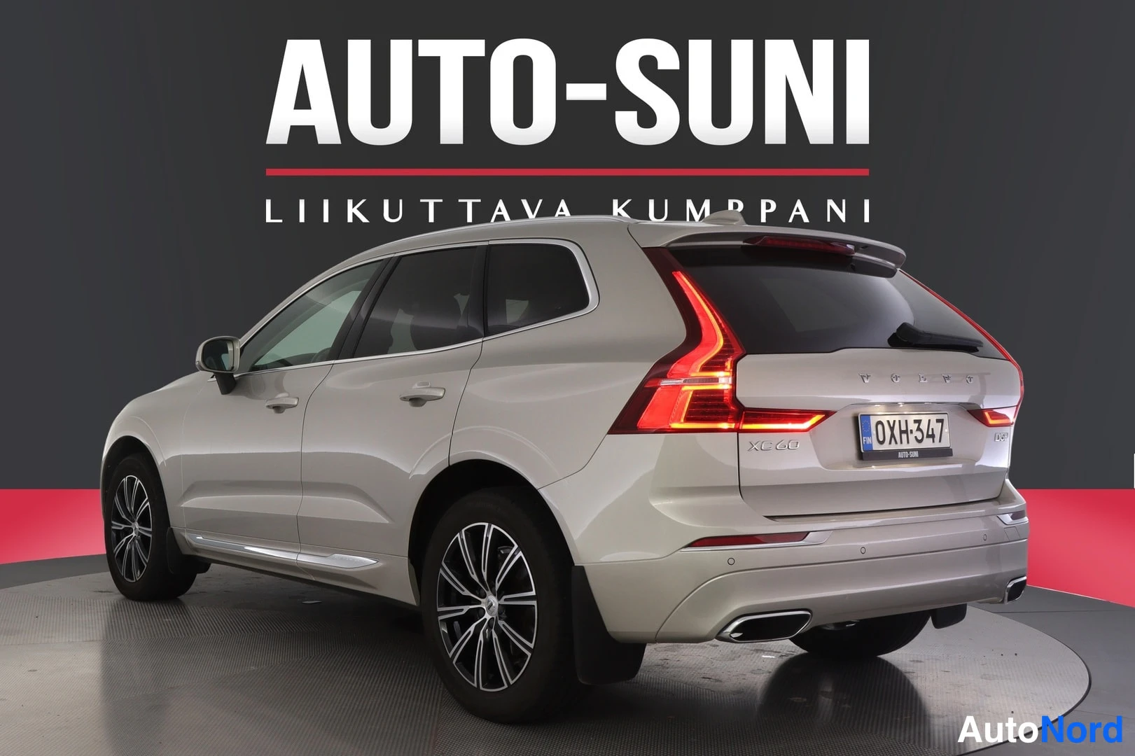 Takaviisto: Beige Volvo XC60:n takakulma oikealta, rekisterikilpi ja taustavalot valaistuna studiotaustaa vasten.