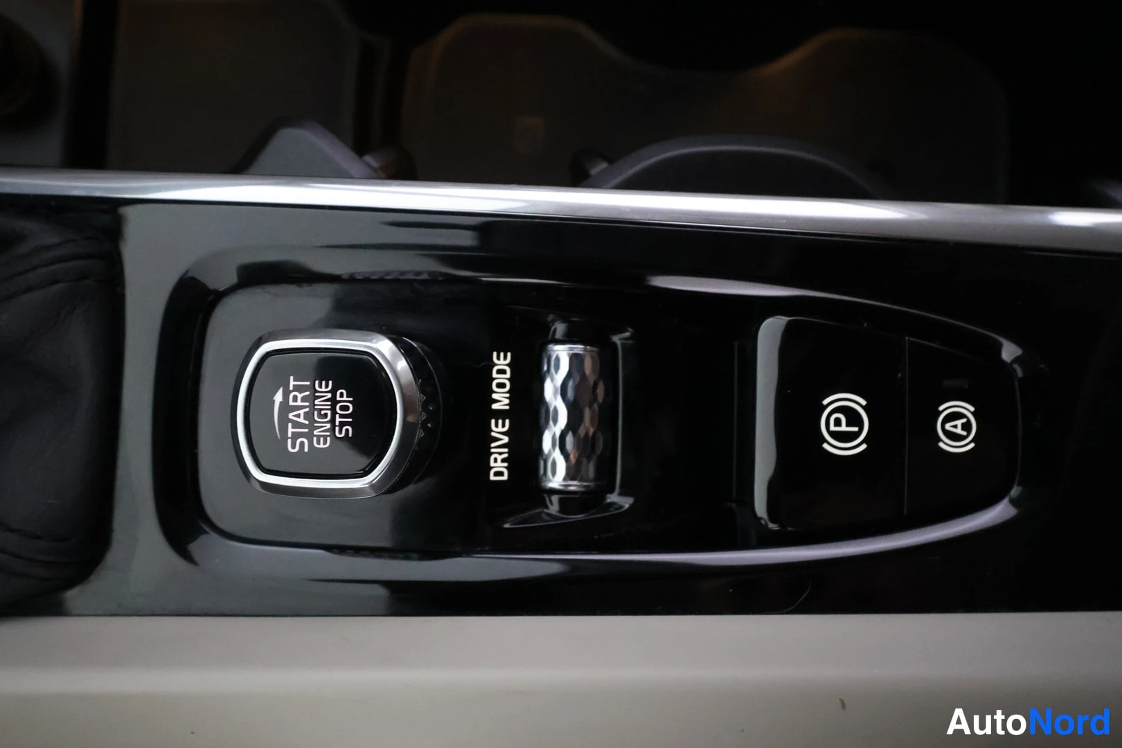 Yksityiskohta: Keskikonsolin kiiltävä musta paneeli: START ENGINE STOP -painike, DRIVE MODE -rulla, sähköisen parkkijarrun (P)-painike ja (A)-merkillä varustettu painike.