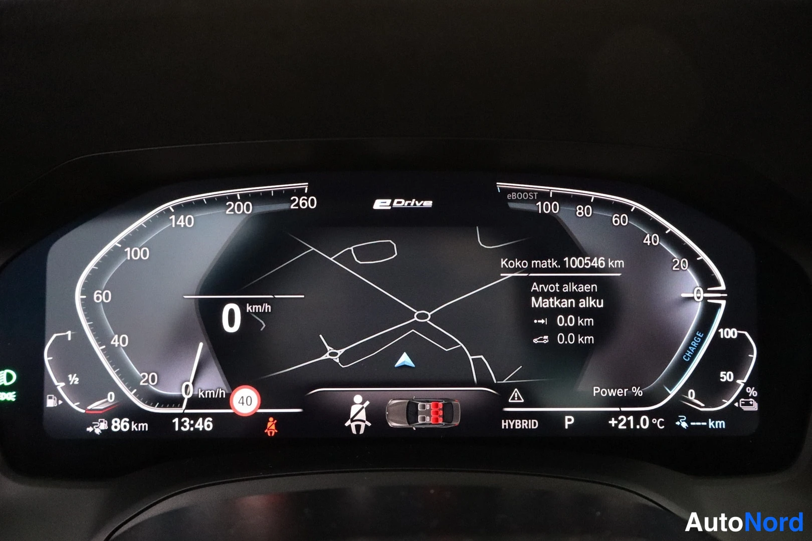 Muu: BMW:n hybridiauton instrumenttinäyttö näkyy nopeusmittarilla (0 km/h), kokonaismatka 100546 km, HYBRID-tila, P-vaihde ja ulkolämpötila +21,0 °C.