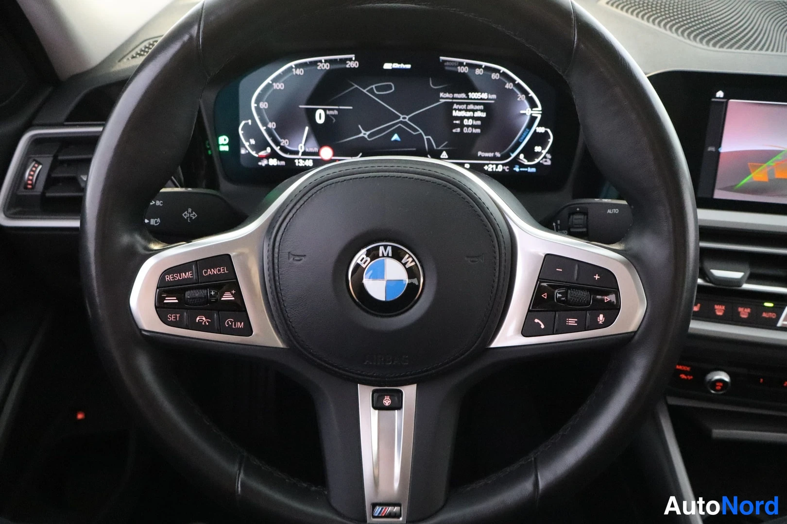 Muu: Ohjauspyörä BMW-merkillä ja M-koristeella, edessä digitaalinen instrumenttinäyttö, jolla kokonaismatka 100546 km, sekä osa keskikonsolin näytöstä.