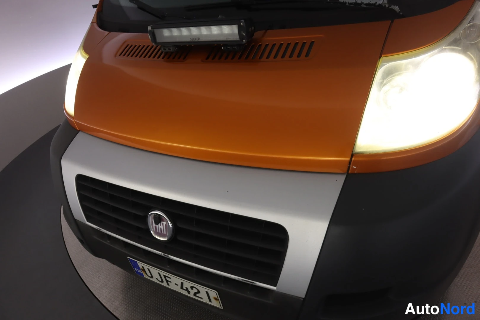 Edestä: Oranssin pakettiauton keula lähikuvana FIAT-merkkiä ja rekisterikilpeä