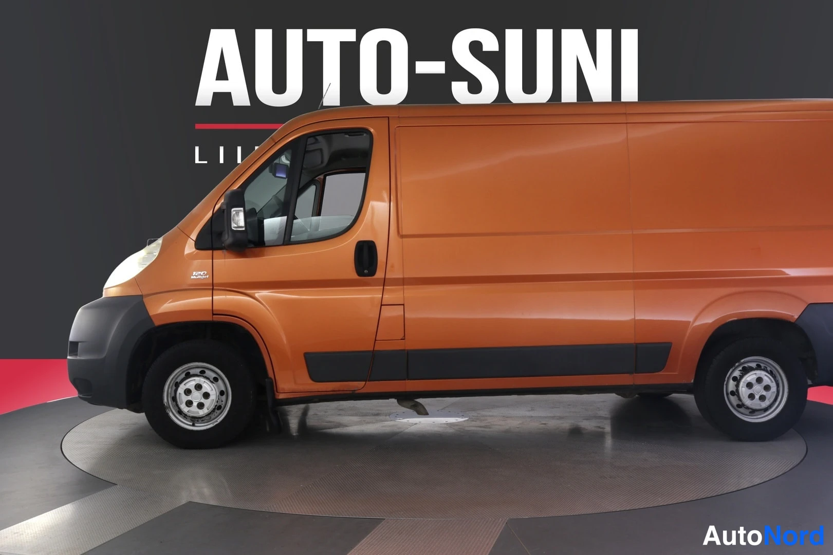 Etuviisto, nokka vasemmalle: Oranssi Fiat Ducato -pakettiauto sivulta etukulmasta, auton keula vasemmalla.