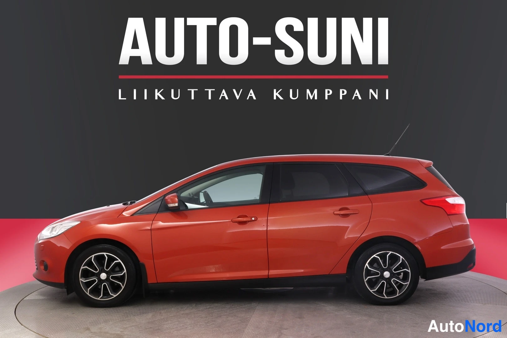 Etuviisto, nokka vasemmalle: Punaisen farmariauton sivuprofiili vasemmalta, mustat vanteet, Auto-Suni-logo taustalla.