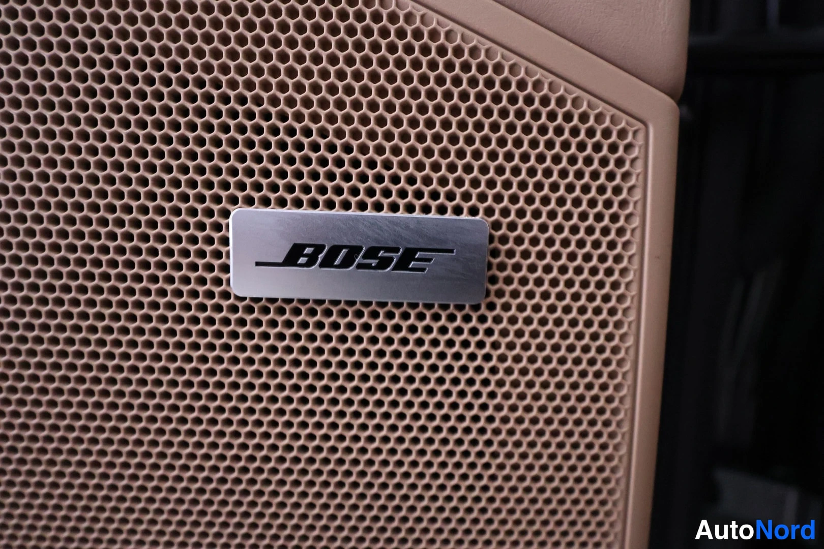 Muu: Bose-kaiuttimen verkkopinta ja Bose-logolla varustettu metallinen kyltti, beigea sisustusta.