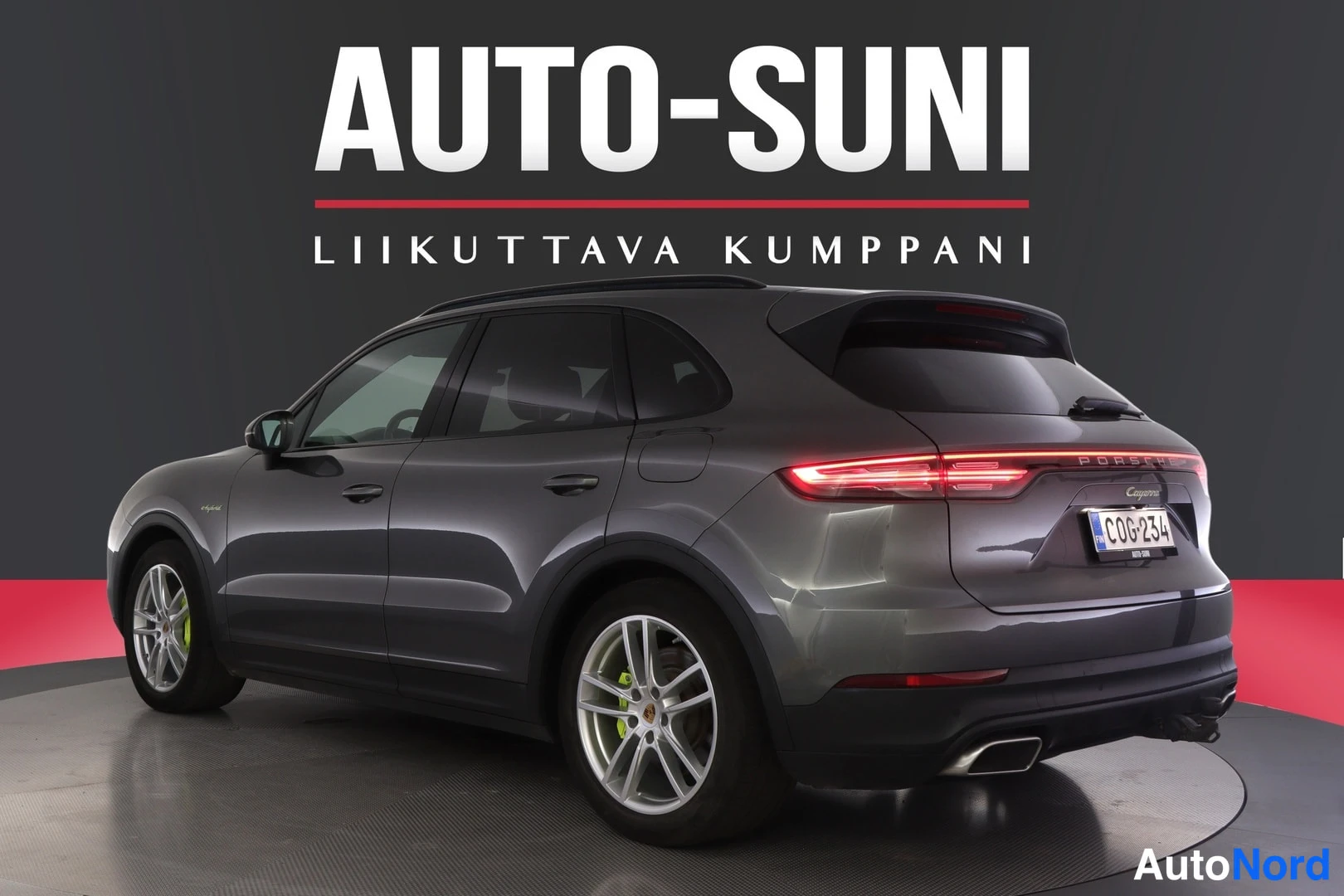 Takaviisto: Porsche Cayenne 2020, tummanharmaa auto takaa vasemmalta kuvattuna, rekisteritunnus, takavalo syttyneenä, taustana AUTO-SUNI-mainos.