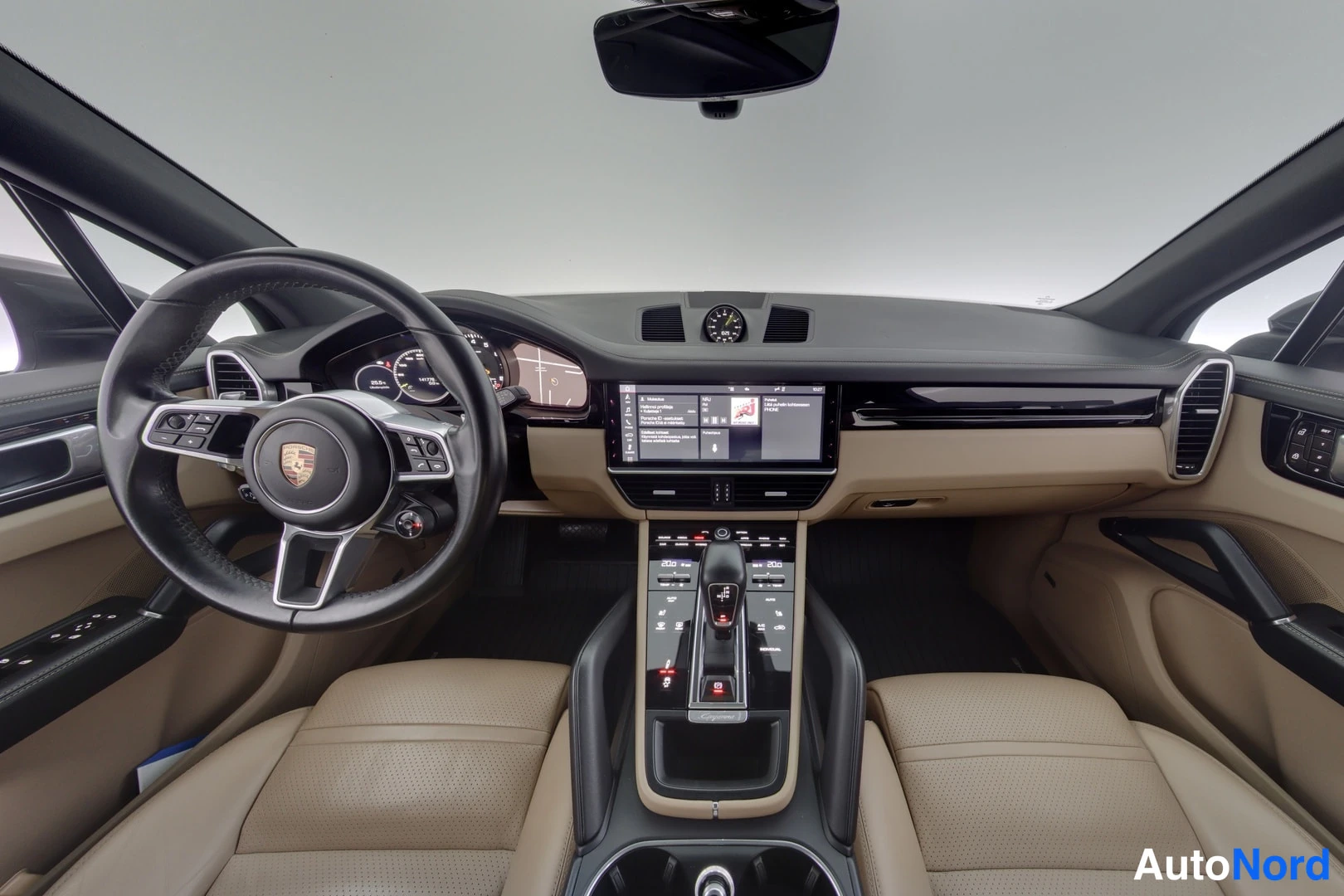 Sivulta: Porsche Cayennen ohjaamo: tumma kojelauta, keskinäinen kosketusnäyttö ja beige nahkaiset etuistuimet.