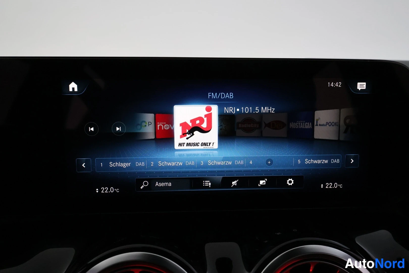 Yksityiskohta: Mercedes-Benzin keskikonsolin infotainment-näyttö, jolla näkyy FM/DAB-radioasema NRJ 101,5 MHz ja kello 14:42