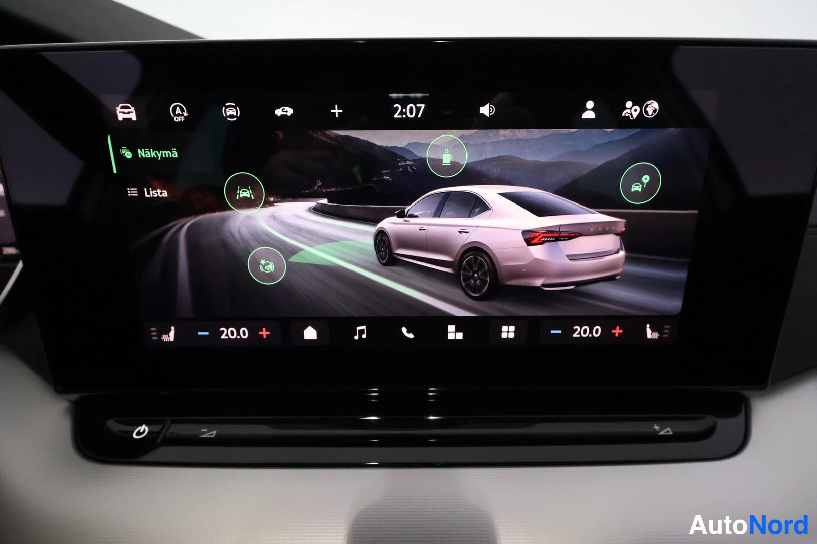 Muu: Infotainment-näyttö lähikuvassa, näkymä 'Näkymä' Listalla, jossa kuvituskuva autosta mutkalla tiellä ja vihrein ympyröin korostettuja toimintokuvakkeita.