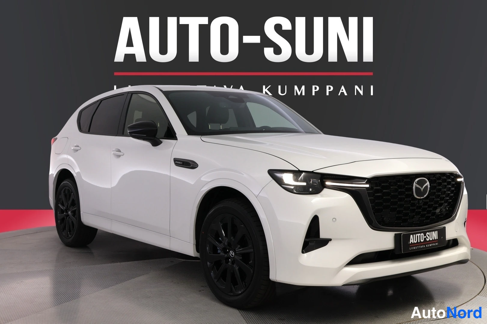 Etuviisto, nokka oikealle: Valkoinen Mazda CX-60 -maasturi kuvattu kolmannelta etunurkalta, keula oikealla, tummat vanteet, myyntitilan tumma tausta.