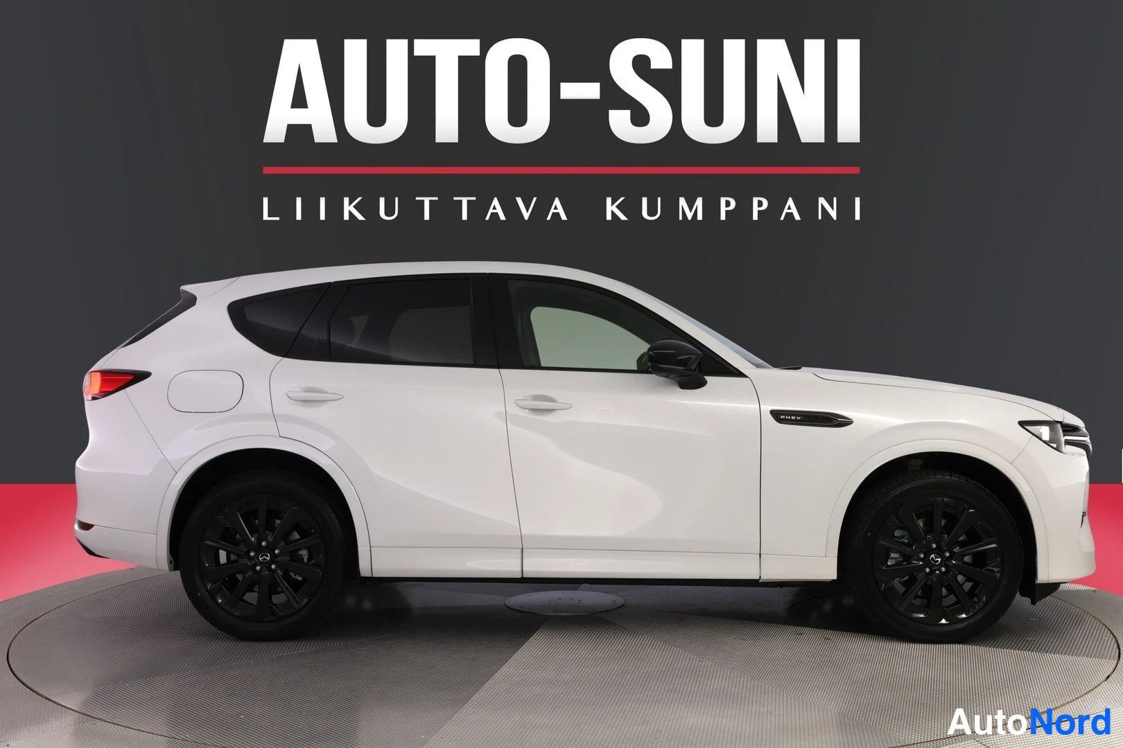 Sivulta: Sivukuva valkoisesta Mazda CX-60 -maasturista, vasen sivu näkyvissä, tummat vanteet, tumma tausta ja punainen lattia-ala.