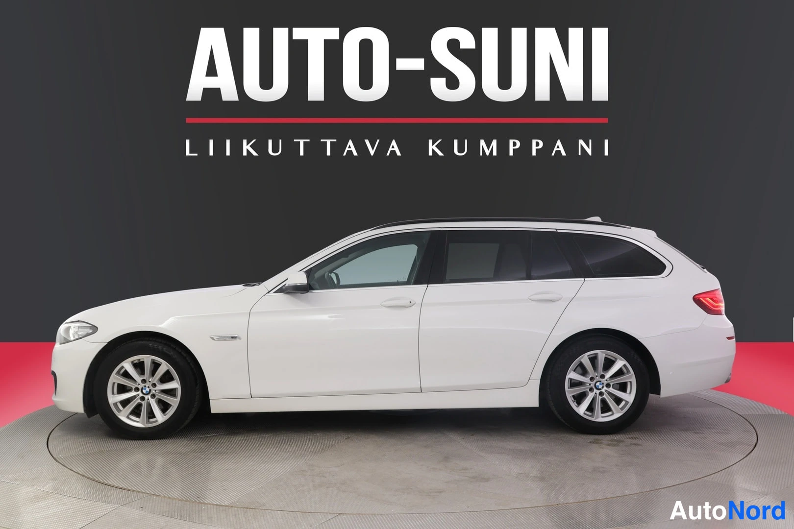 Sivulta: Valkoinen farmariauto sivulta vasemmasta etukulmasta, myymälätaustassa teksti Auto-Suni.